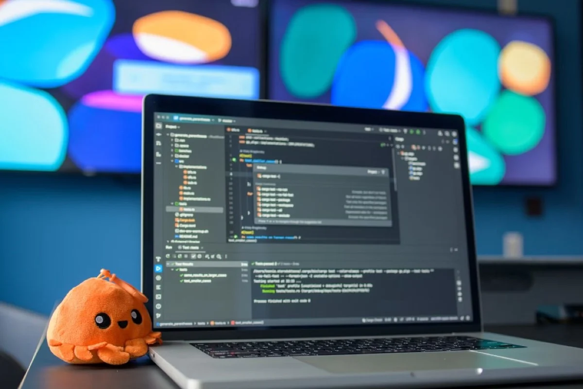 Laptop with passing tests on screen and a small desk mascot at a workspace