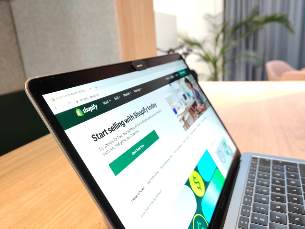 Laptop on a wooden desk showing a Shopify storefront in the browser
